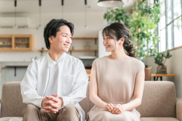 家のリビングでソファーに座る若い夫婦