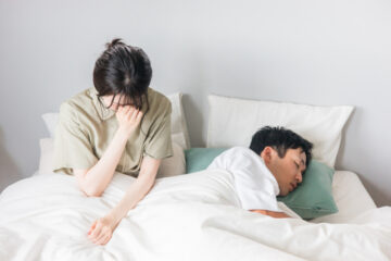 ベッドの上で悩んでいる女性と寝ている男性